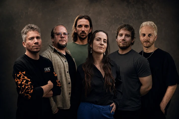 The six members of Lesoir standing together against a dark, textured backdrop